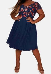 Námořnické šaty s květinovou krajkovou bodicí, krátkými rukávy a skládací sukní. Mají výstřih do V a jemnou, lehkou texturu.