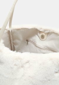 Borsa a spalla in finta pelliccia di un morbido color crema con un interno liscio, dotata di una tasca con zip e una chiusura a scatto magnetico. Manici in materiale abbinato.