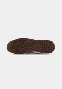Shoe sole in brown rubber with circular grip patterns; features a purple and white upper with a classic lace design and prominent branding.