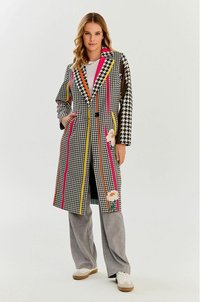Płaszcz w wzór houndstooth w czerni i bieli, ozdobiony kolorowymi pasami w odcieniach różu, pomarańczy i żółci, z haftem kwiatowym i kieszeniami.