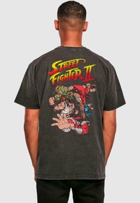 Sort bomulds T-shirt med et livligt grafisk motiv af "Street Fighter II" karakterer på ryggen. Korte ærmer og rund halsudskæring.