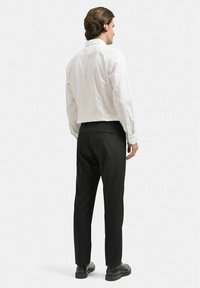 Vit skjorta med knappar för män, långärmad, med bakstycke, och svarta byxor i slätt tyg. Svarta skor kompletterar outfitet.