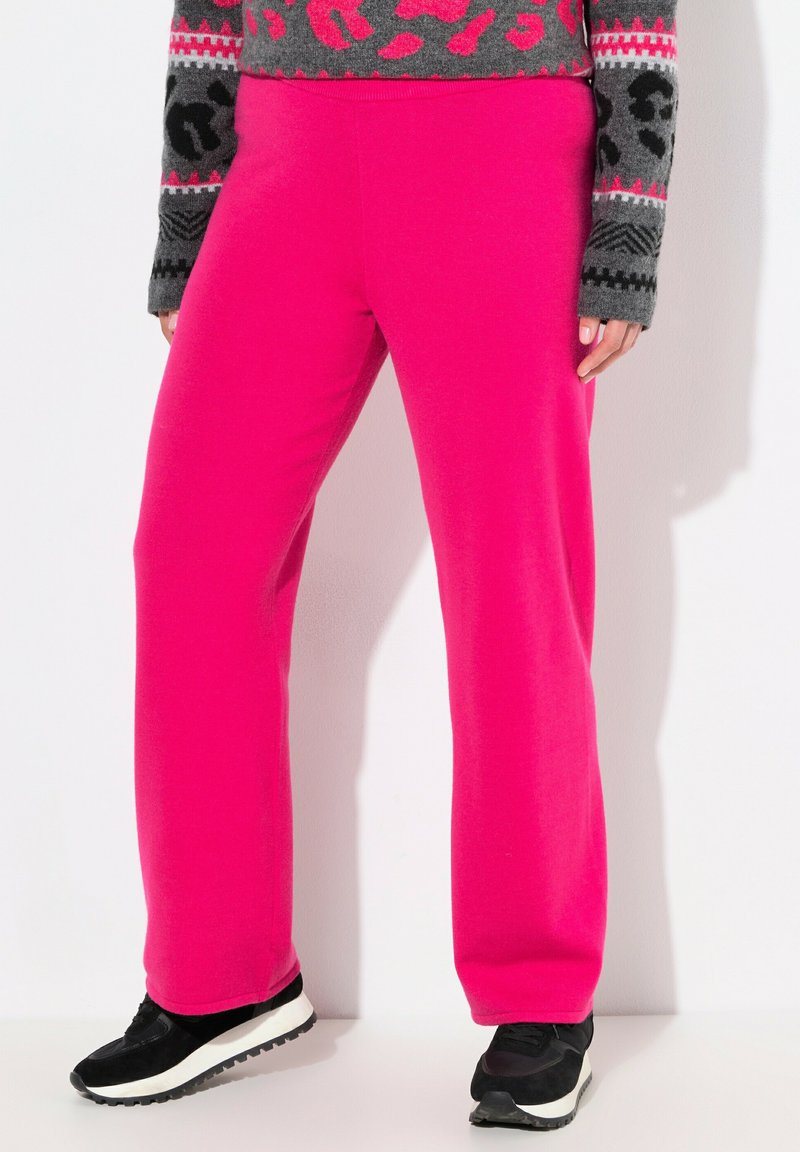 Fuksia venytyshousut, joissa on rento istuvuus, sileä pinta ja joustava vyötärönauha, yhdistettynä mustiin urheilukenkiin ja kuvioituun harmaaseen neuleeseen.