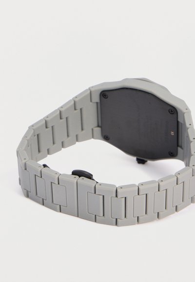 Γκρι μεταλλικό μπρασελέ ρολογιού με συνδεδεμένα τμήματα, προσαρτημένο σε μαύρη θήκη ρολογιού, απεικονίζεται σε λευκό φόντο.