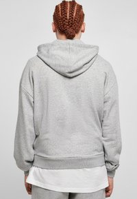 Grijze hoodie met een ruime capuchon, losse pasvorm, geribbelde manchetten en zoom. De textuur lijkt zacht, gecombineerd met een wit gelaagd shirt eronder.