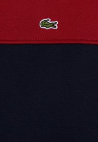 Rot und marineblaues Strick-Polohemd aus strukturiertem Stoff mit kontrastierenden Farben und einem kleinen grünen gestickten Krokodil-Logo auf der linken Seite.