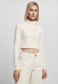 Cremfarbener, kurz geschnittener Langarm-Pullover mit Rollkragen aus glattem Stoff. Verfügt über ein figurbetontes Design mit einem dezenten grünen Logodetail am Saum.