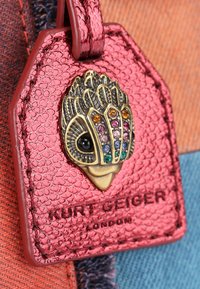 Roze textuur leren label met een metallic accentontwerp, versierd met kleurrijke juwelen en een reliëflogo "Kurt Geiger London."