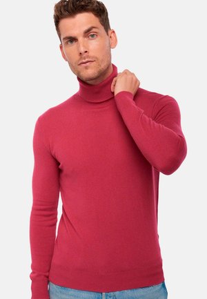 Un pull col roulé rouge en maille douce, doté de manches longues et d'un design ajusté, présenté sur un modèle devant un fond uni.