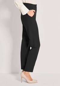 Schwarze maßgeschneiderte Hose mit geradem Schnitt und Seitentaschen, kombiniert mit hellbeigen High Heels, die einen eleganten, professionellen Look präsentieren.