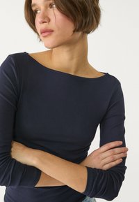 Navy pitkähihaiset paita, jossa on leveä kaula-aukko, slim fit -leikkaus, pehmeä kangas ja istuvat hihat. Paidan muotoilussa on siisti viimeistely ja vähäiset yksityiskohdat.