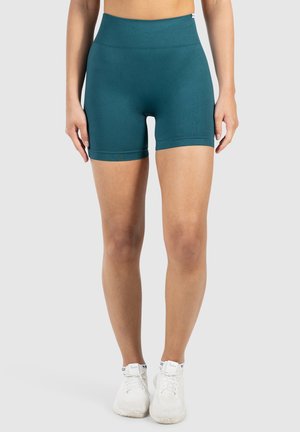 Teal sportshorts met een hoge elastische tailleband; gladde textuur en fitted vorm; gedragen met witte sportschoenen.
