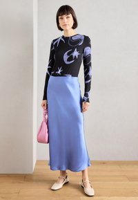 Μαύρη μπλούζα με μακριά μανίκια και μοβ αφηρημένα σχέδια, συνδυασμένη με μία λεία, μακριά σατέν φούστα σε ανοιχτό μπλε χρώμα και μπεζ παπούτσια. Ροζ τσάντα ώμου.