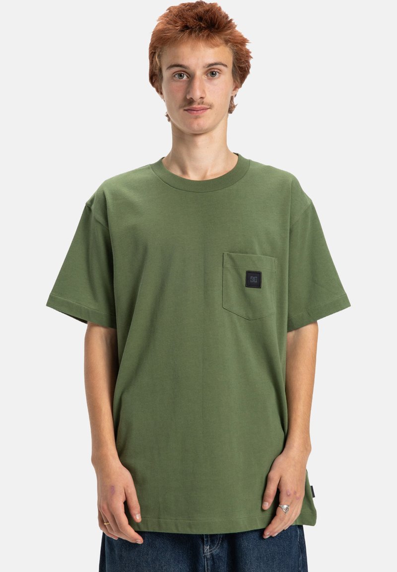 Zelené bavlněné tričko s kulatým výstřihem, krátkým rukávem a kapsou na prsou s černou nálepkou. Volný střih a hladká textura.