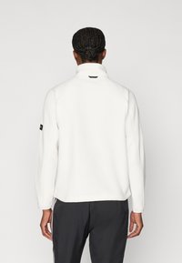 Λευκό φλις πουλόβερ με ψηλό γιακά, ραγάδες μανίκια, υφή υφάσματος και διακριτική λεπτομέρεια λογότυπου στο αριστερό μανίκι.