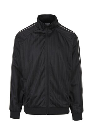 Veste de sport noire zippée intégrale avec col haut, motif vertical subtil, poignets et ourlet côtelés, et fines bandes blanches le long des épaules et des manches.