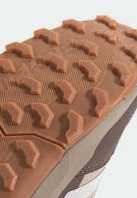 Podešev boty v barvě světle hnědé s výraznými gumovými výstupky pro lepší přilnavost, s texturovanými vzory a hladkými okraji, rámovaná hnědou boční částí.