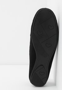 Chaussure noire à enfiler avec une semelle en caoutchouc texturée présentant des accents en forme de cœur et un design flexible. Taille indiquée : 37.