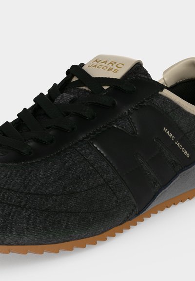Baskets Marc Jacobs gris foncé et noires avec lacets noirs, étiquette beige sur la languette et détail de semelle en caoutchouc naturel, vues de profil et de face.