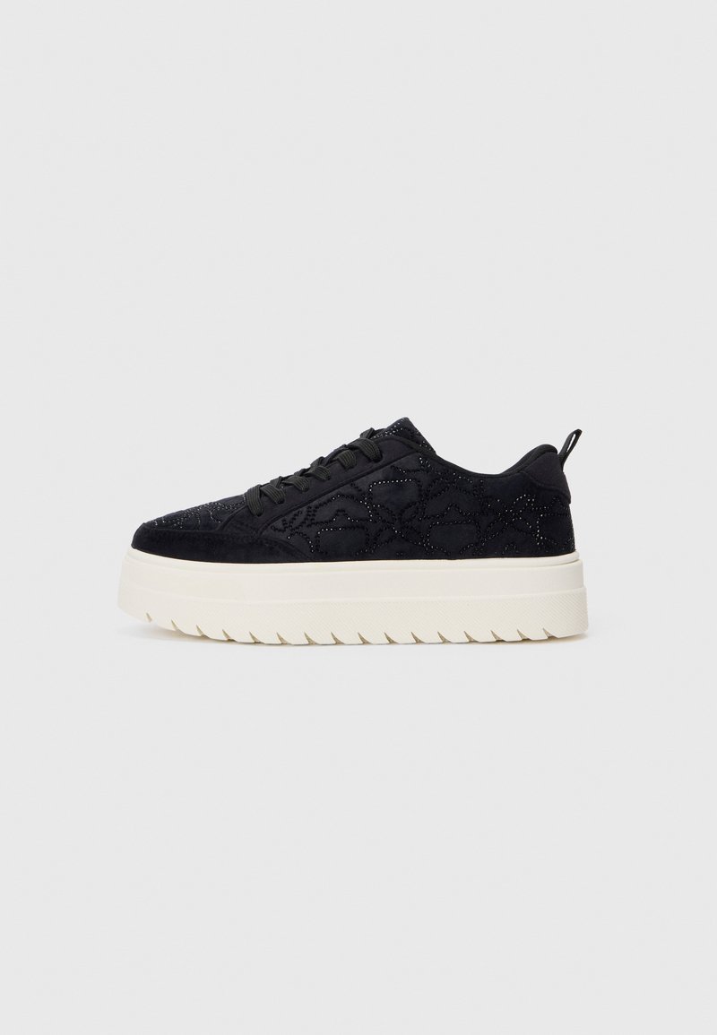 Adidași negri din suede cu cusături decorative, șireturi negre și talpă din cauciuc alb, cu un model ondulat, pe un fundal simplu deschis.