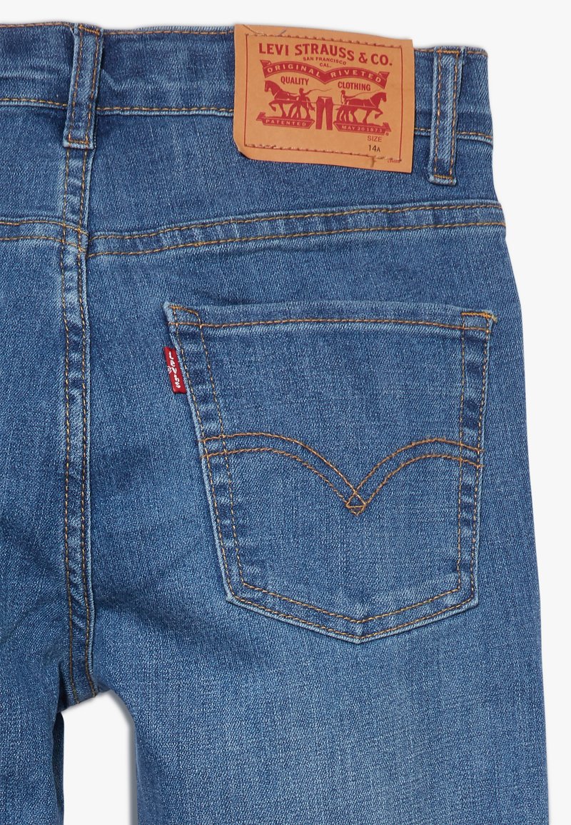 Lichtblauwe denim jeans met contrasterende gele stiksels, een tan leren achterpatch en een kenmerkend rood etiket op de linkerzak.
