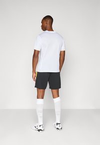 Hvid atletisk t-shirt med korte ærmer, parret med sorte shorts og hvide knæstrømper, der har sorte og hvide fodboldstøvler.