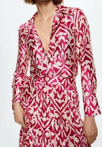 Blouse imprimée avec un motif abstrait rose et blanc, dotée d'un décolleté en V, de manches longues et d'un design plissé à la taille.