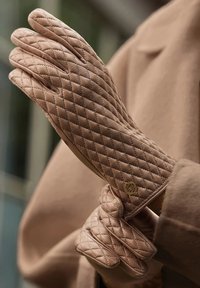 Quilted beige gloves with a diamond pattern, featuring a gold logo accent near the cuff, made from a soft leather material.