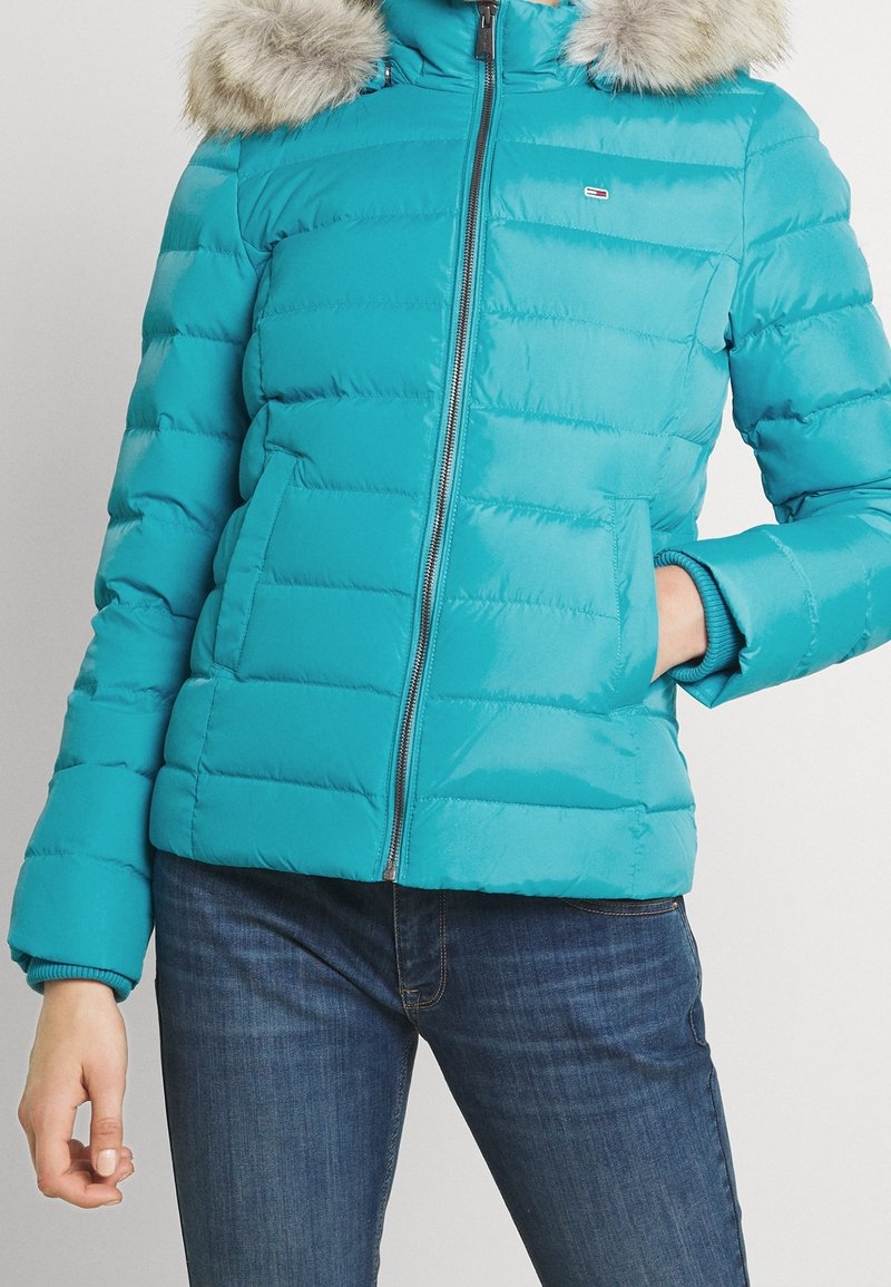 Turquoise donsjack met horizontale stiksels, ritssluiting en afneembare nepbontkraag. Voorzien van zijzakken en geribbelde manchetten.