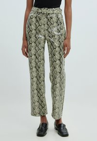 Hooggewaste, glanzende groene en beige slangenprint broeken met een ceintuur in de taille en rechte pijpen, gecombineerd met zwarte loafers.
