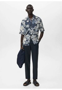 Cămașă cu mânecă scurtă, de culoare bleumarin, cu modele florale albe, combinată cu pantaloni bleumarin și sandale negre. Modelul ține o jachetă bleumarin.
