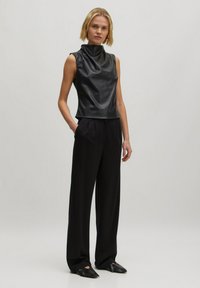 Zwart faux leren mouwloos topje met hoge halslijn, gecombineerd met zwarte wijde broek en zwarte puntige instapschoenen.