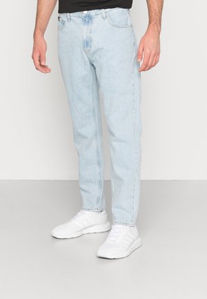 Jeans de denim azul claro con corte recto, diseño de cinco bolsillos y un leve desgaste, combinados con zapatillas blancas.