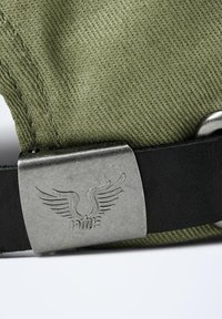 Casquette en tissu vert olive avec une surface texturée ; dotée d'une boucle en métal argenté avec un logo d'aile et un détail de sangle noire.