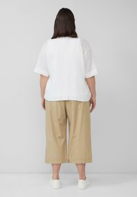 Witte linnen top met korte mouwen, gecombineerd met beige cropped broeken en witte schoenen, gezien vanaf de achterkant tegen een neutrale achtergrond.