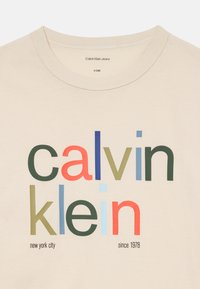 Bežs T-krekls ar daudzkrāsainu "calvin klein" tekstu, zemāk ar mazāku melnu tekstu "new york city" un "since 1978".