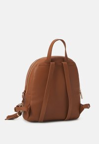 Brauner Leder-Rucksack mit strukturiertem Finish, zwei Schulterriemen, einem oberen Griff und goldfarbener Reißverschluss-Details. Kompaktes, rundes Design.