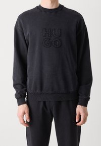 Sudadera negra hecha de una tela suave, con un logo texturizado "HUGO" en el frente, cuello acanalado y puños y dobladillo elásticos.