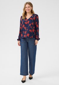 Marinblus med röd blommönster, V-ringning, lång ärm. Kombinerad med vida denimjeans i blått och svarta spetsiga skor.