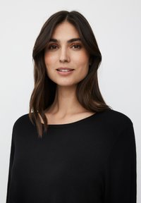 Maglione nero a maglia con scollo ampio e maniche lunghe, caratterizzato da una texture liscia e una vestibilità comoda, indossato da una donna con capelli di lunghezza media.