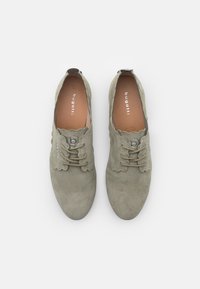 Zapatos de ante gris claro con puntera redondeada, bordes con forma de onda y dos cierres de cordones. La plantilla presenta el nombre de la marca "bugatti."