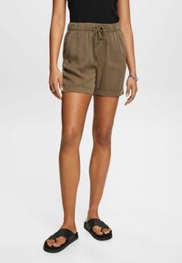 Vihreät, kevyet shortsit, joissa on elastinen vyötärö, nyöri, kaksi sivutaskua ja käärityt lahkeet. Yhdistetty mustiin sandaaleihin.