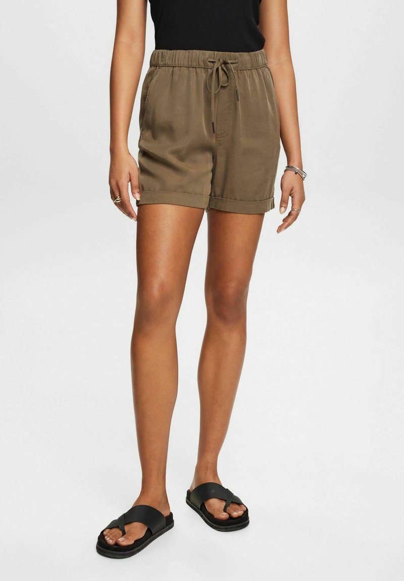 Vihreät, kevyet shortsit, joissa on elastinen vyötärö, nyöri, kaksi sivutaskua ja käärityt lahkeet. Yhdistetty mustiin sandaaleihin.