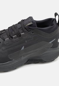Les chaussures noires Nike Trail ATC présentent une tige texturée avec un marquage Gore-Tex, des lacets ronds et une semelle à motifs pour l'adhérence et la durabilité.