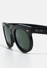 Ochelari de soare din plastic negru cu lentile verzi închise. Au un design îndrăzneț, cu o ramă supradimensionată și logo-ul argintiu Ray-Ban pe braț.
