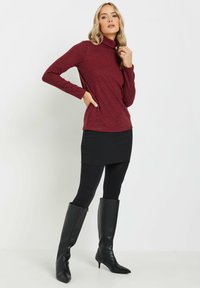 Bourgognefärgad polotröja i mjukt material, kombinerad med en svart minikjol och svarta knähöga stövlar. Outfiten har lång ärm och en slim fit.