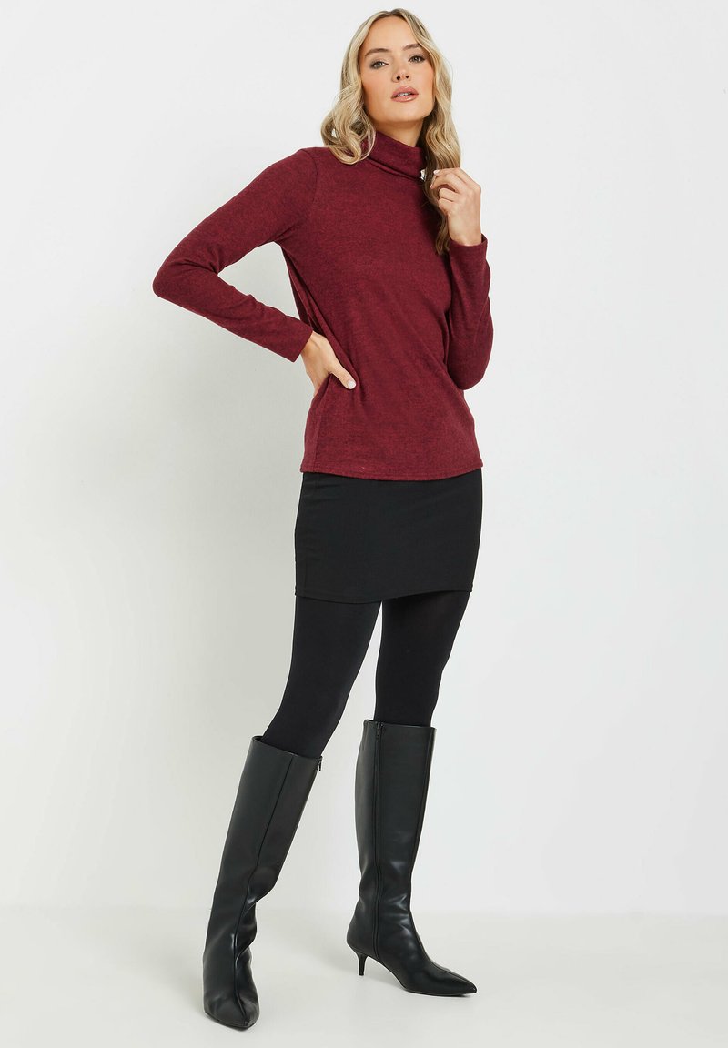 Bourgognefärgad polotröja i mjukt material, kombinerad med en svart minikjol och svarta knähöga stövlar. Outfiten har lång ärm och en slim fit.