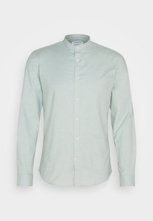 Jasnozielona koszula z długim rękawem, z kołnierzykiem stójkowym, zapinana na guziki, o miękkiej fakturze. Posiada zaokrąglony dół i standardowe mankiety.