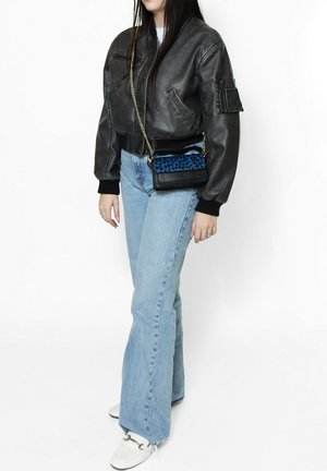 Giacca bomber in pelle nera con polsini a costine, jeans svasati blu chiaro e una piccola borsa nera con un accento a stampa leopardo blu.