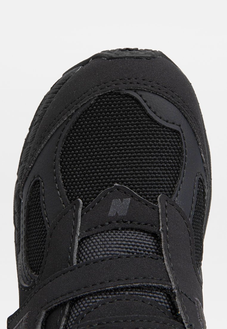 Chaussure de sport noire avec une tige en maille et des accents texturés, une sangle en Velcro et un col rembourré, conçue pour le confort et le soutien.